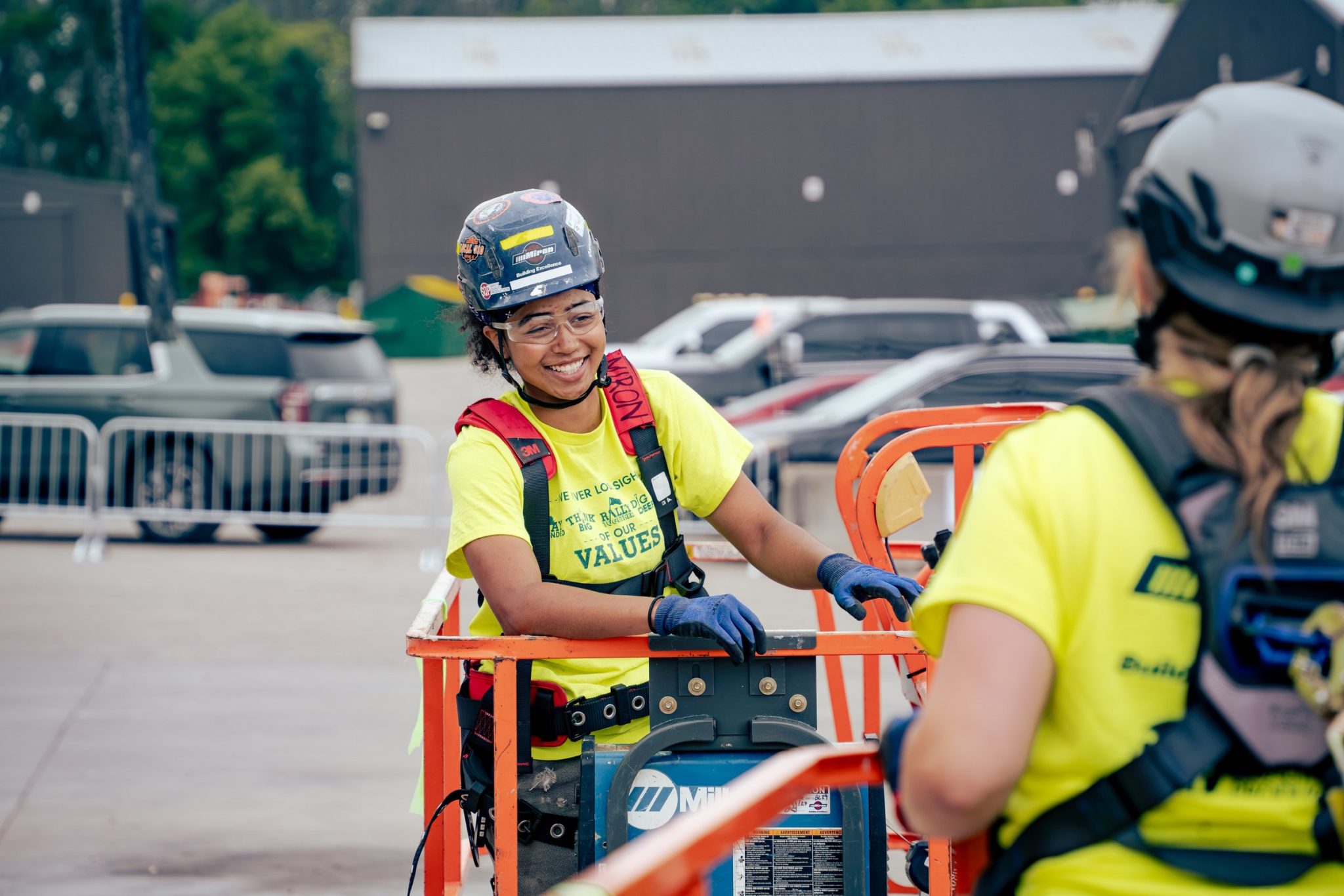 A smiling Miron crew member in a hard hat and safety harness on an aerial lift