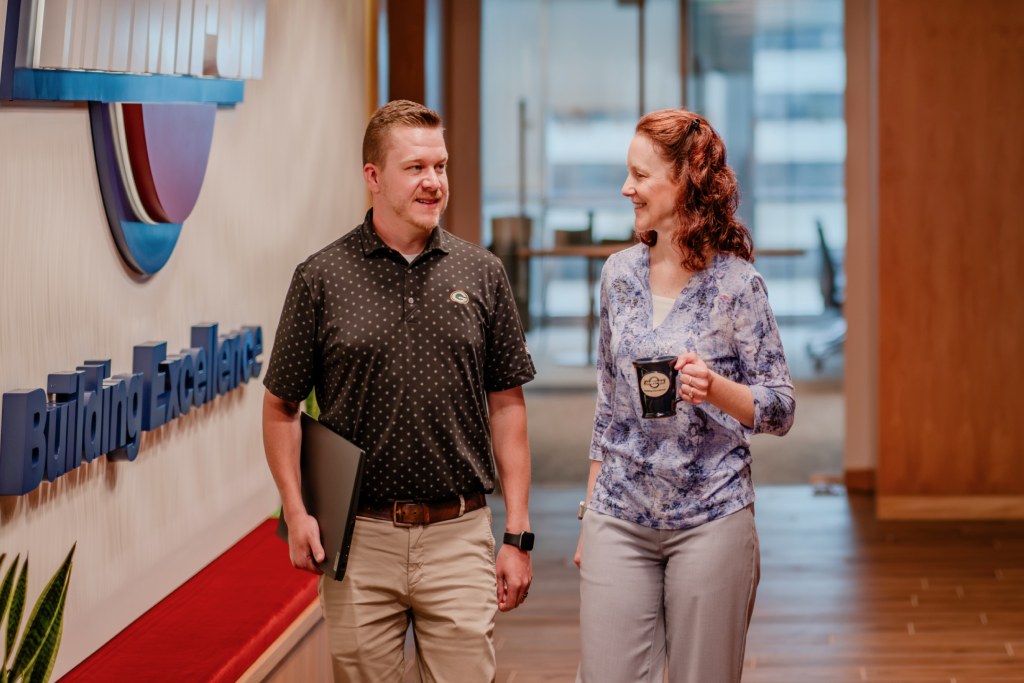 Two Miron office employees walking and talking past the Building Excellence wall