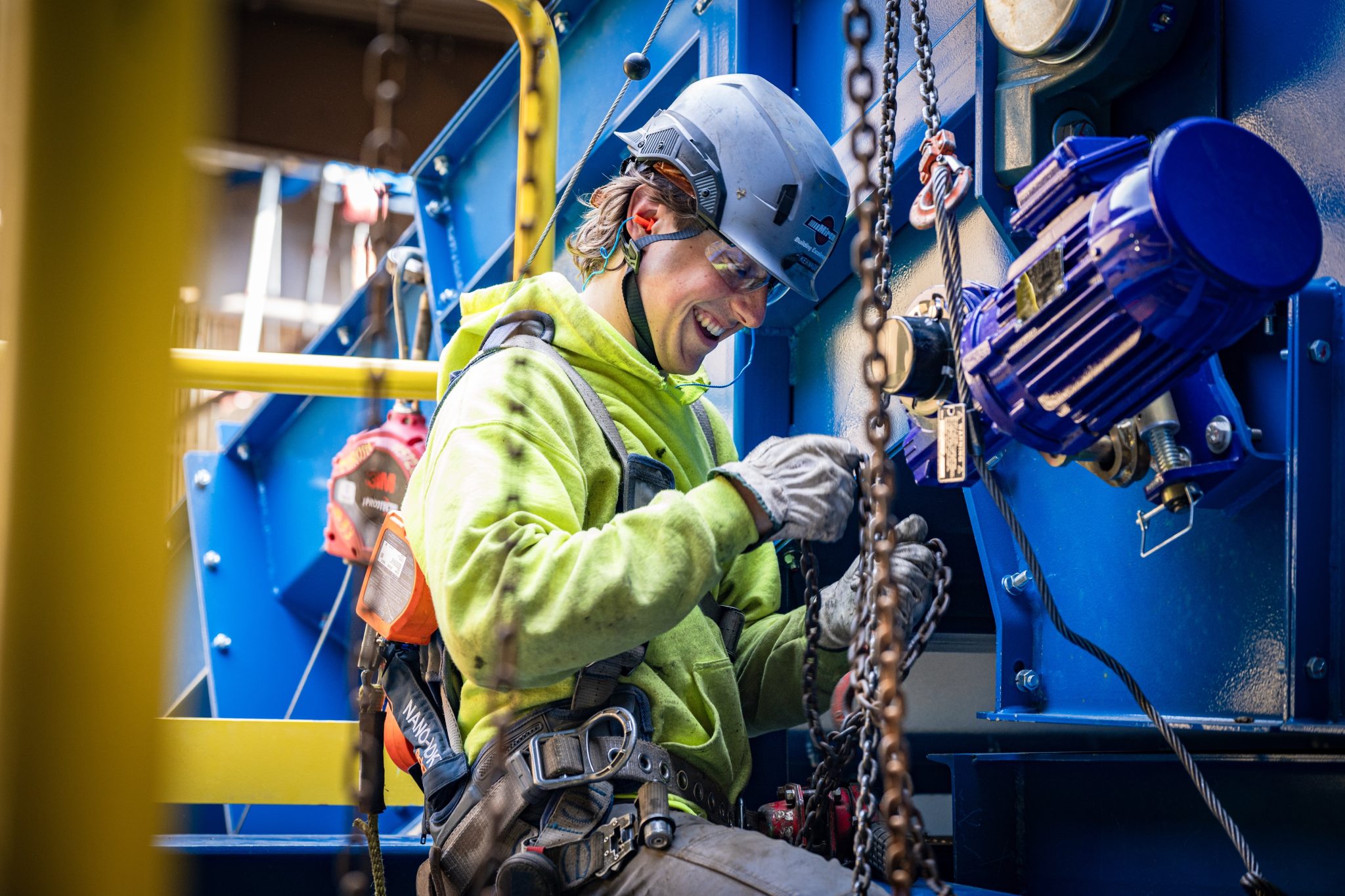 Smiling Miron field worker in a hard hat rigging chain on blue equipment