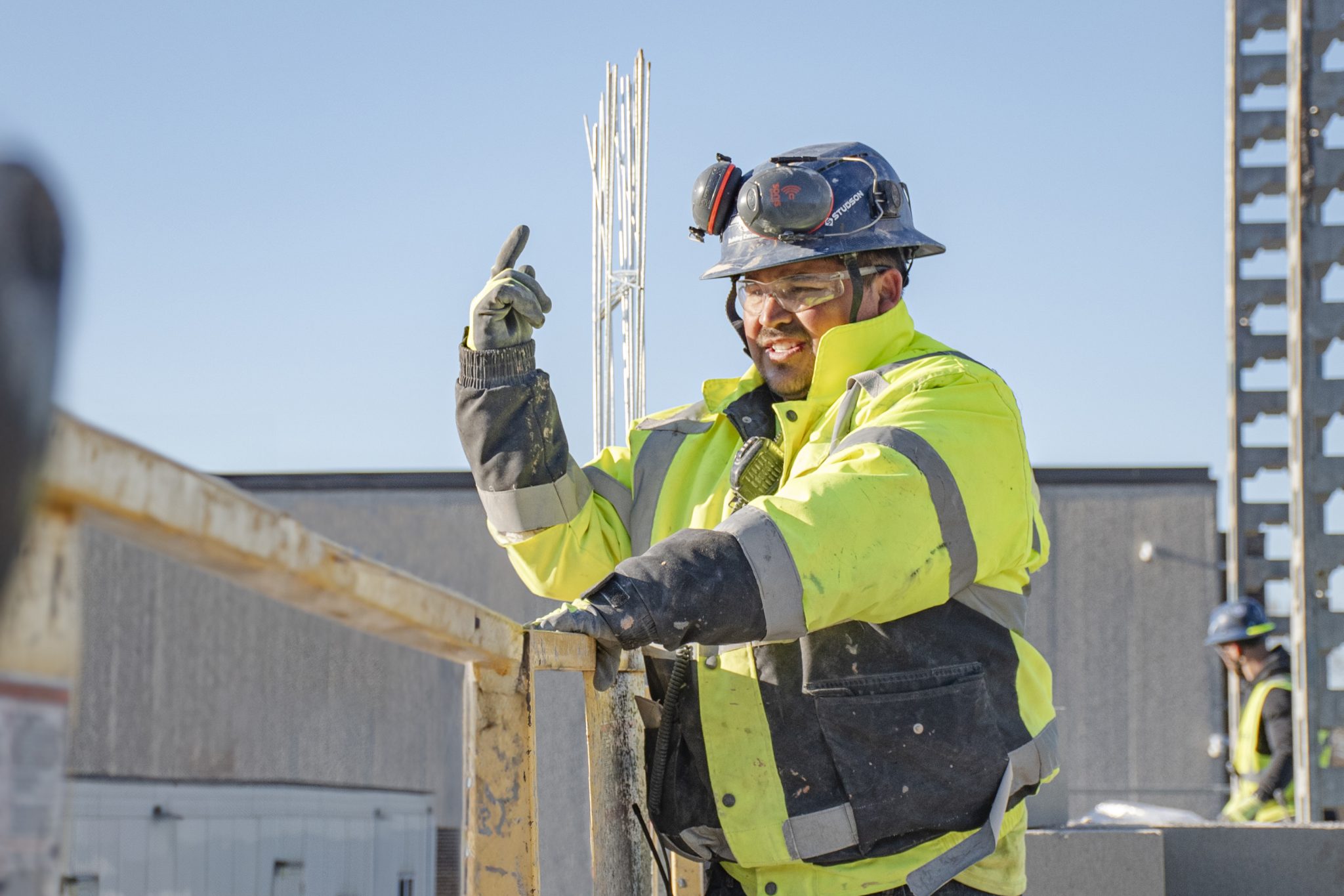 Smiling Miron craftsperson pointing upward on a jobsite
