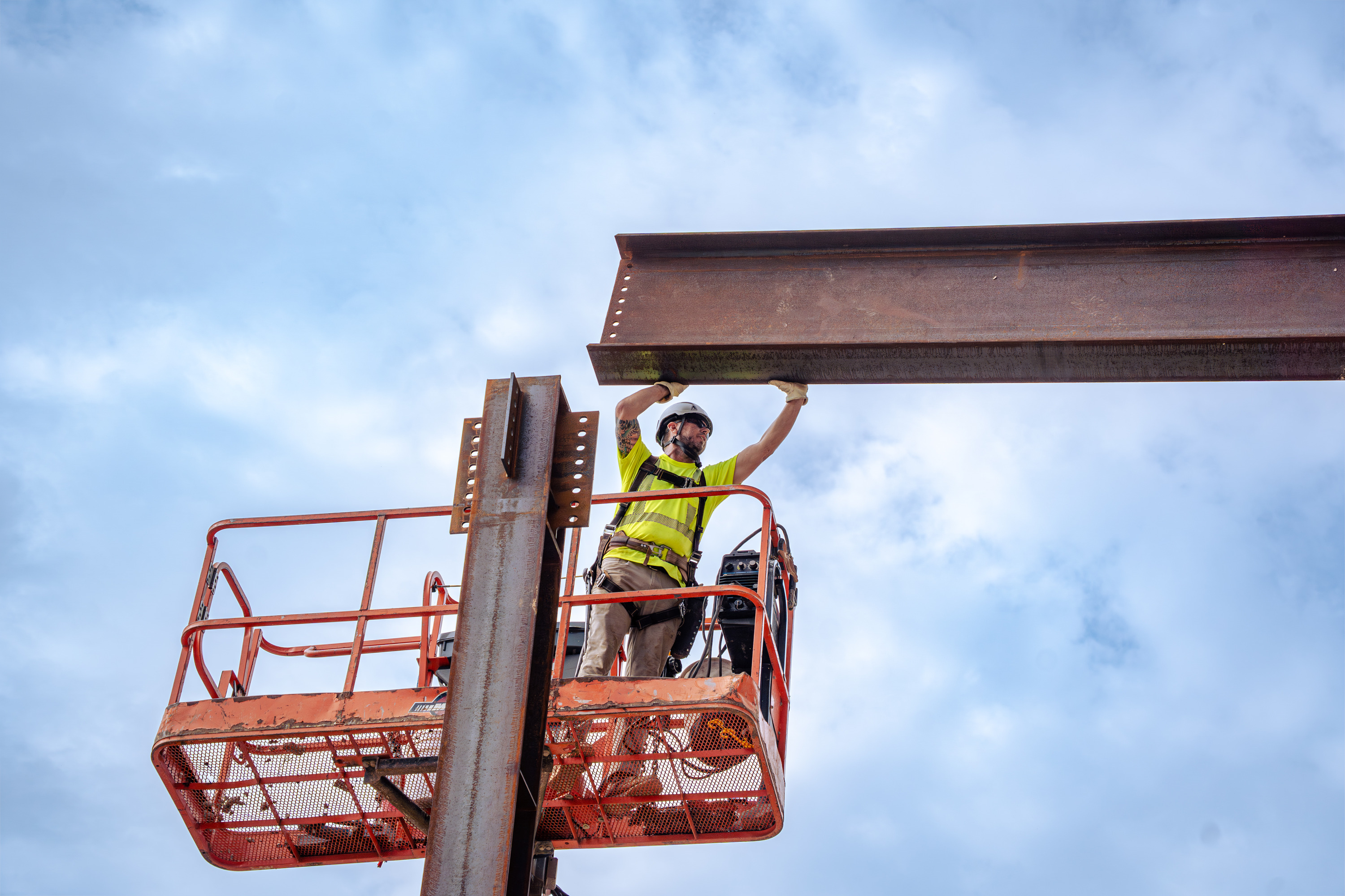 Youth apprentice in a lift guiding a steel beam into place