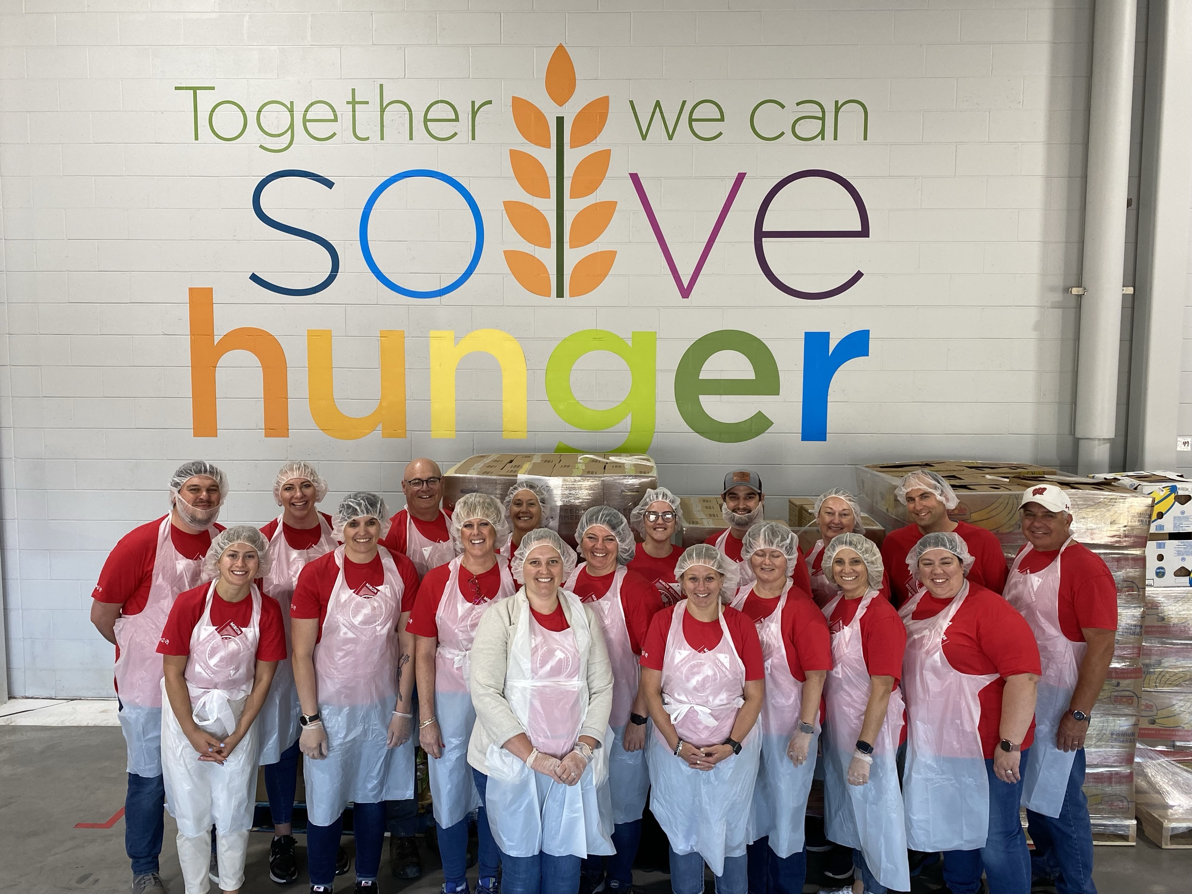 Miron volunteers in hairnets and aprons under a Together We Can Solve Hunger mural