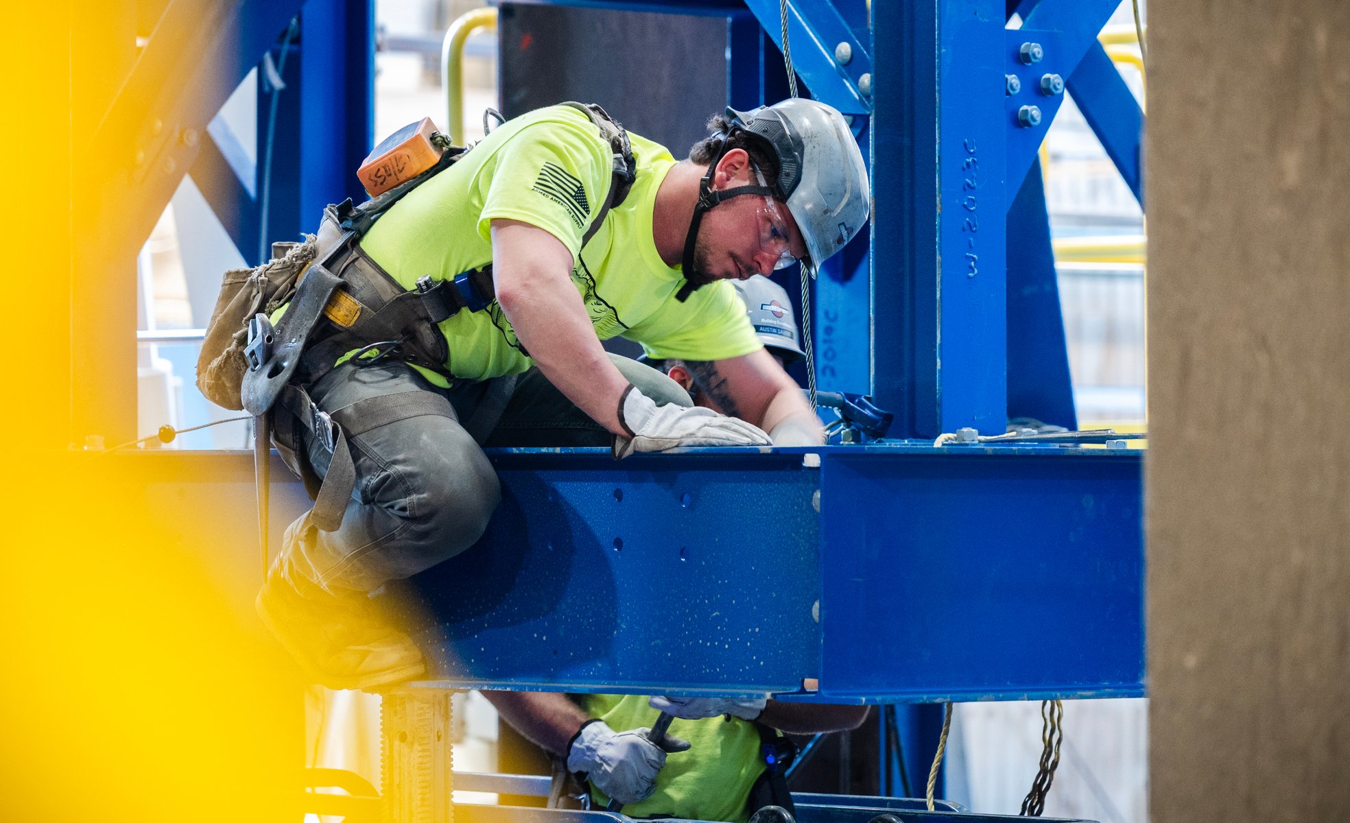 A Miron ironworker apprentice in a harness bolting a blue steel beam